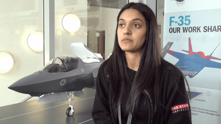Mid-shot of a female facing off camera left stood in front of a model of an F-35 aircraft.